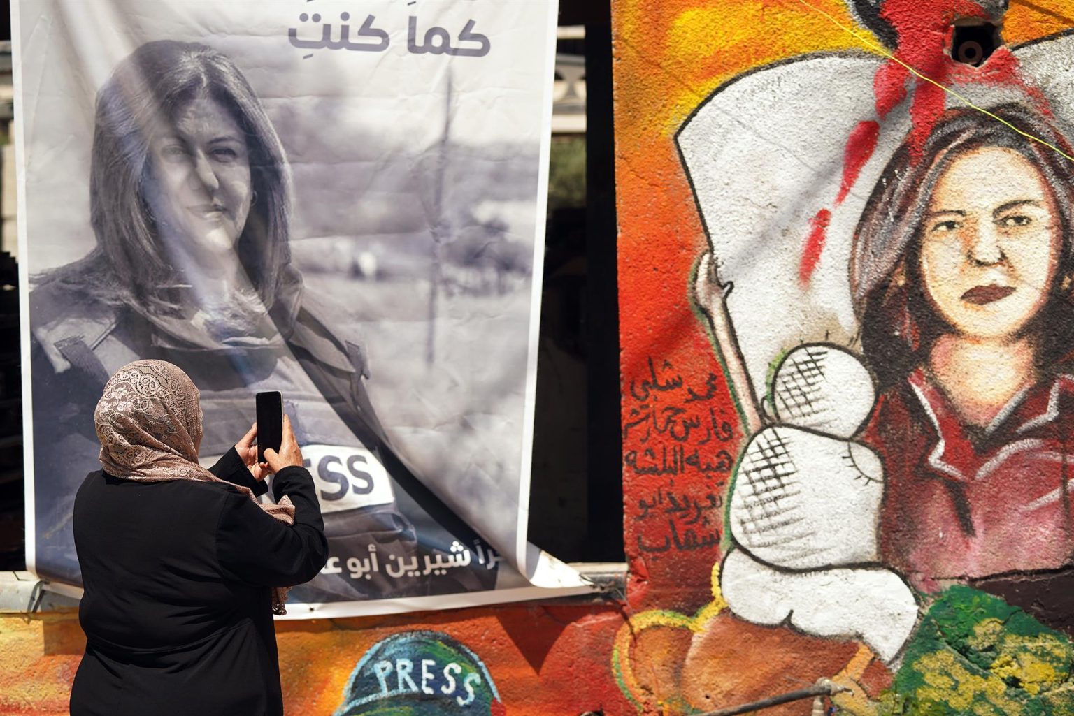 Una mujer toma fotos de un retrato y un mural en memoria de la periodista de Al Yazira Shireen Abu Akleh, que conforman un improvisado altar al que los palestinos acuden a rezar y rendirle homenaje, en Yenín, Cisjordania. Imagen de archivo. EFE/ Sara Gómez Armas