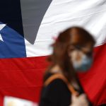 Una mujer camina frente a una bandera de Chile en Santiago (Chile). EFE/ Alberto Valdés