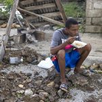 Un hombre come sentado sobre unos escombros tras el paso del huracán Fiona en el barrio Ginandiana, en El Seibo (República Dominicana). EFE/ Orlando Barría