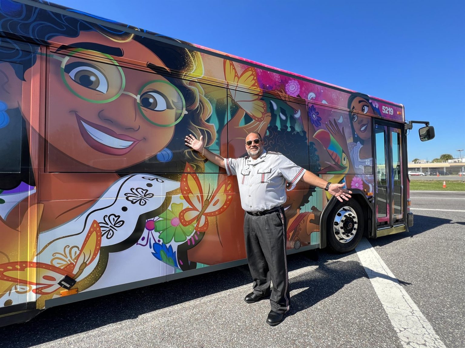 Fotografía cedida por Disney donde se muestra a un conductor mientras señala a un autobús decorado con personajes de la película "Encanto". Los visitantes de Disney World, el complejo de parques temáticos de Disney en Orlando (Florida), se desplazarán estos días por sus instalaciones a bordo de autobuses decorados con motivos de la película animada "Encanto" para honrar el Mes de la Herencia Hispana. EFE/Disney /SOLO USO EDITORIAL /NO VENTAS /SOLO DISPONIBLE PARA ILUSTRAR LA NOTICIA QUE ACOMPAÑA /CRÉDITO OBLIGATORIO