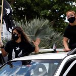 Imagen de archivo que muestra a dos personas vestidas de negro ondeando la bandera puertorriqueña en negro desde las ventanas de un auto en San Juan (Puerto Rico). EFE/Thais Llorca