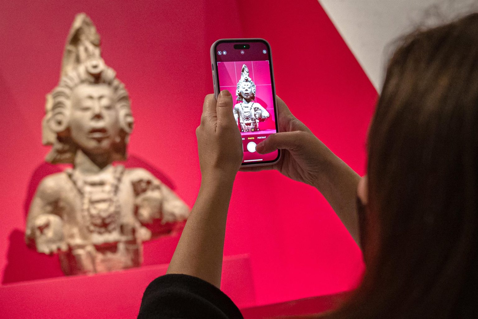 Una mujer toma una foto con su teléfono móvil a una obra en piedra caliza representando al Dios del maíz (del Templo 22, Copán, Honduras) durante una visita de prensa a la exposición "Vida de los dioses: la divinidad en el arte maya" hoy, en el Museo Metropolitano (MET) en Nueva York (EEUU). EFE/Ángel Colmenares