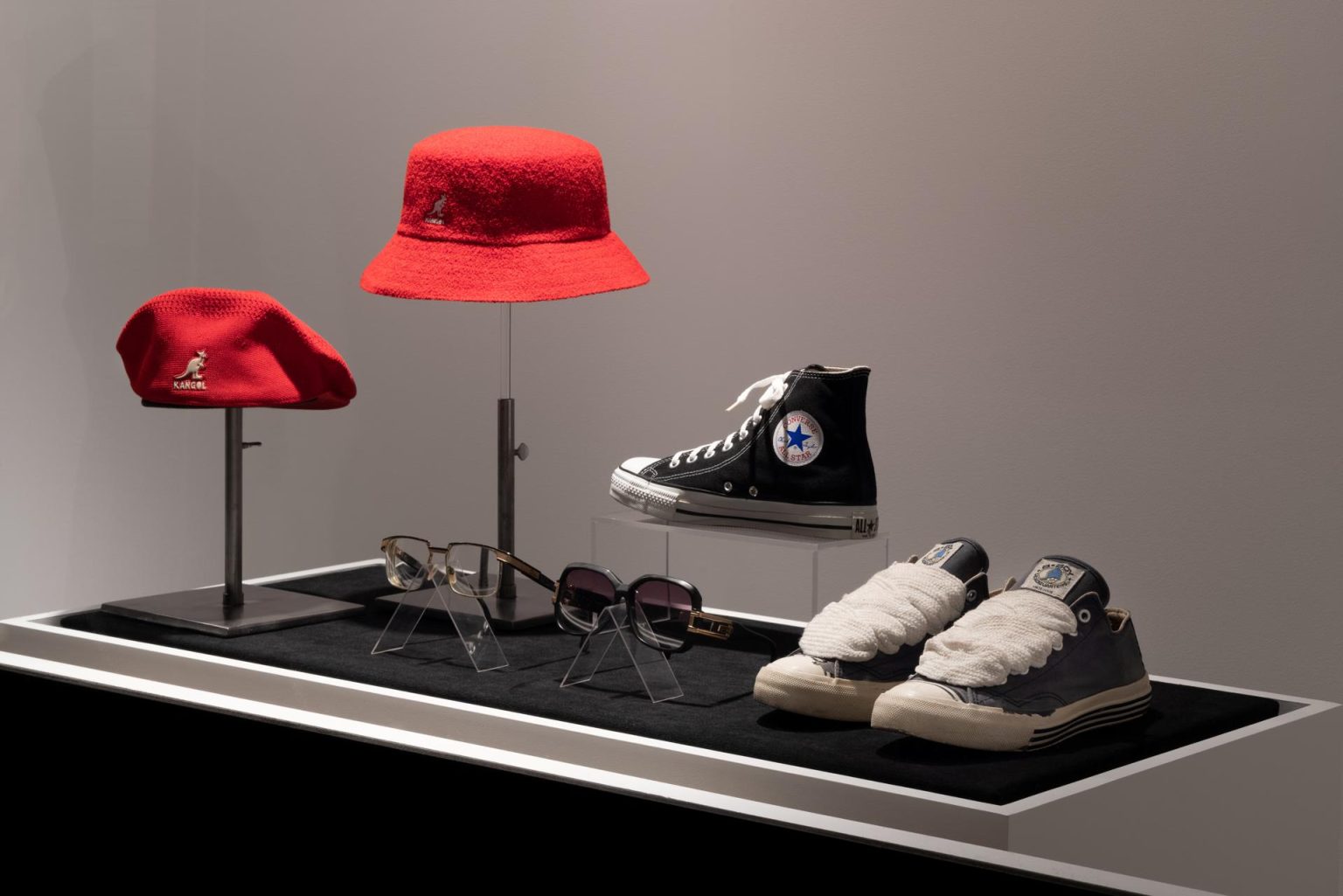 Fotografía sin fecha cedida por el Museo del Instituto de Tecnología de la Moda de Nueva York (FIT) donde se aprecia (desde la izquierda) una gorra Kangol de los años 80-90, prestada por Claudia Gold; un sombrero de pescador Kangol del 2022, prestado por Eileen Costa; unas gafas Cazal de los años 70-80, prestadas por Jamel Shabazz; unas gafas Cazal de los años 70-80, prestadas por Claudia Gold; unas  zapatillas Converse de 1999, regalo de Converse Inc., y unas zapatillas deportivas Pro-Keds con cordones gruesos personalizados de 1978, prestadas por Clemente Moreno alias Niño Congelado, mostrados en la exhibición "Fresh, Fly, and Fabulous: Fifty Years of Hip Hop Style" en la sede del museo ubicado en la séptima avenida de Nueva York (EEUU).  El FIT inauguró este miércoles la exposición más grande y completa sobre el estilo revolucionario e influyente del hip hop, que celebra el 50 aniversario de su nacimiento, y marca la primera vez que esta institución explora la moda exclusivamente a través de un género musical. EFE/Eileen Costa/FIT /SOLO USO EDITORIAL /NO VENTAS /SOLO DISPONIBLE PARA ILUSTRAR LA NOTICIA QUE ACOMPAÑA /CRÉDITO OBLIGATORIO