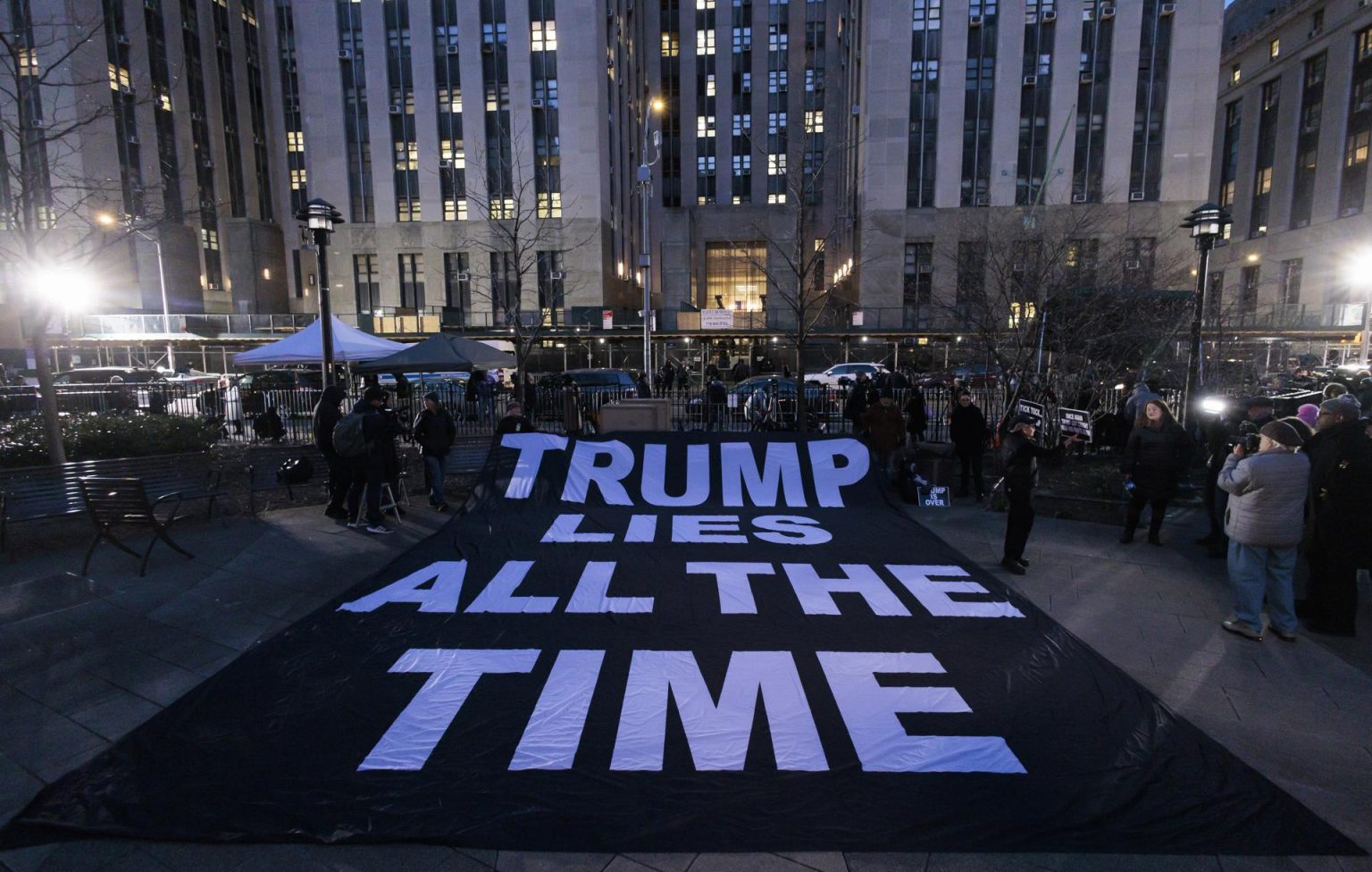 La gente despliega un cartel en el que se lee en inglés "Trump miente todo el tiempo" al otro lado de la calle del edificio de la Corte Penal de Nueva York, poco después de la acusación del ex presidente Donald J. Tump, en Nueva York (EE.UU.). EFE/ Justin Lane