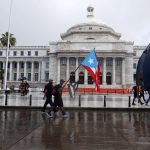 Unas personas con banderas nacionales caminan frente al Capitolio, de la Cámara de Representantes y el Senado en San Juan (Puerto Rico). Imagen de archivo. EFE/Thais Llorca