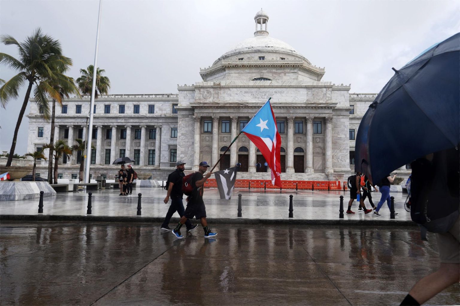 Unas personas con banderas nacionales caminan frente al Capitolio, de la Cámara de Representantes y el Senado en San Juan (Puerto Rico). Imagen de archivo. EFE/Thais Llorca