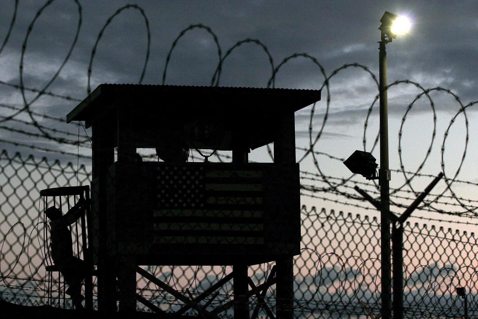 Fotografía de archivo que muestra la silueta de un miembro de la Fuerza de Tarea Conjunta (i) subiendo a una garita junto a un alambrado en un perímetro de seguridad en Campo Delta, estación naval en Guantánamo (Cuba). EFE/JOHN RILEY