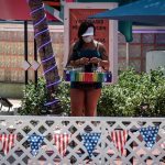 Una mujer usa tapabocas mientras vende tabaco y mecheros en el paseo turístico de Ocean Drive en Miami Beach, Florida. EFE/Giorgio Viera