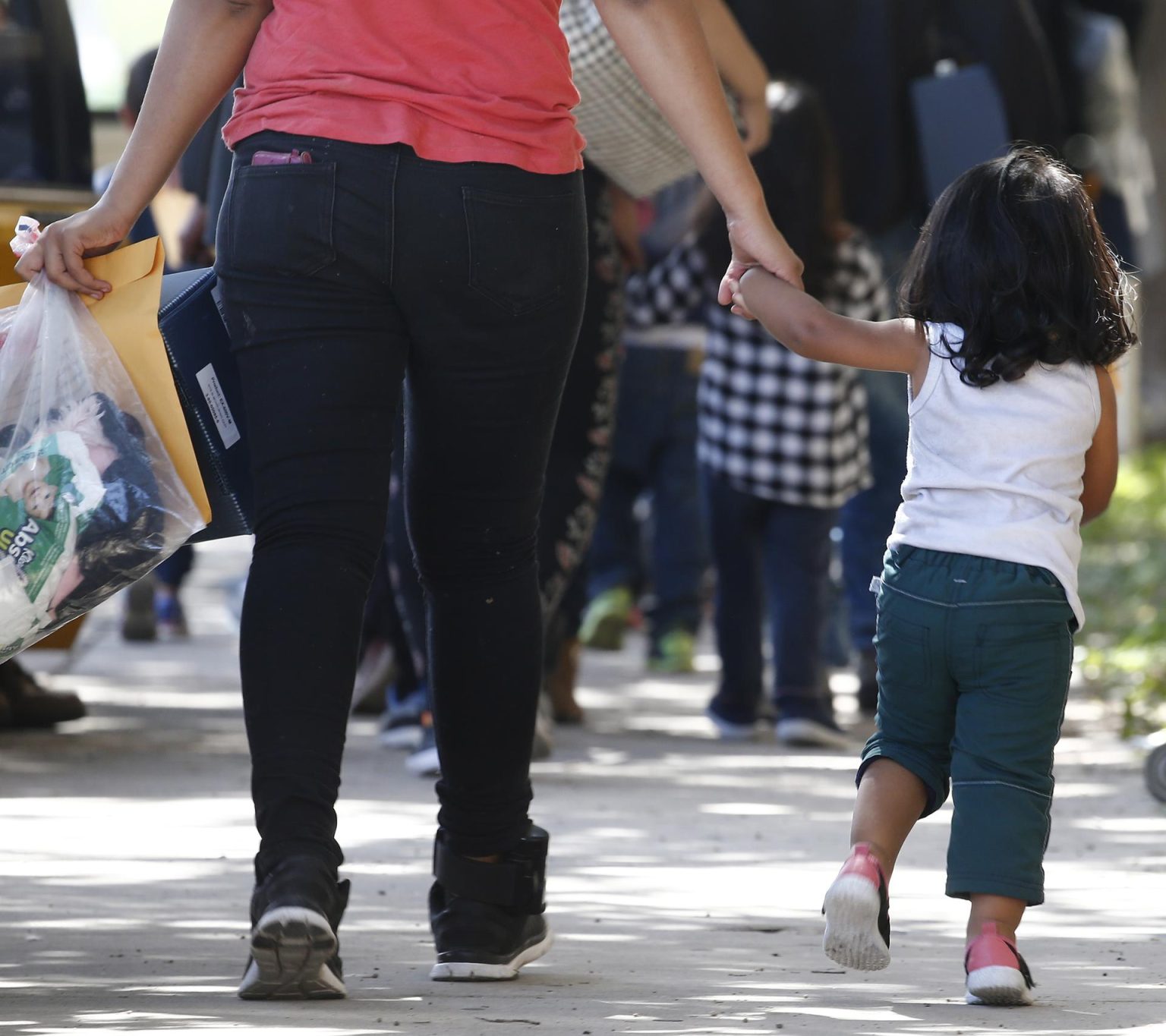 Familias migrantes cruzan la calle después de ser procesados en la estación central de autobuses antes de ser llevados a Caridades Católicas en McAllen, Texas (EE.UU.). EFE/LARRY W. SMITH