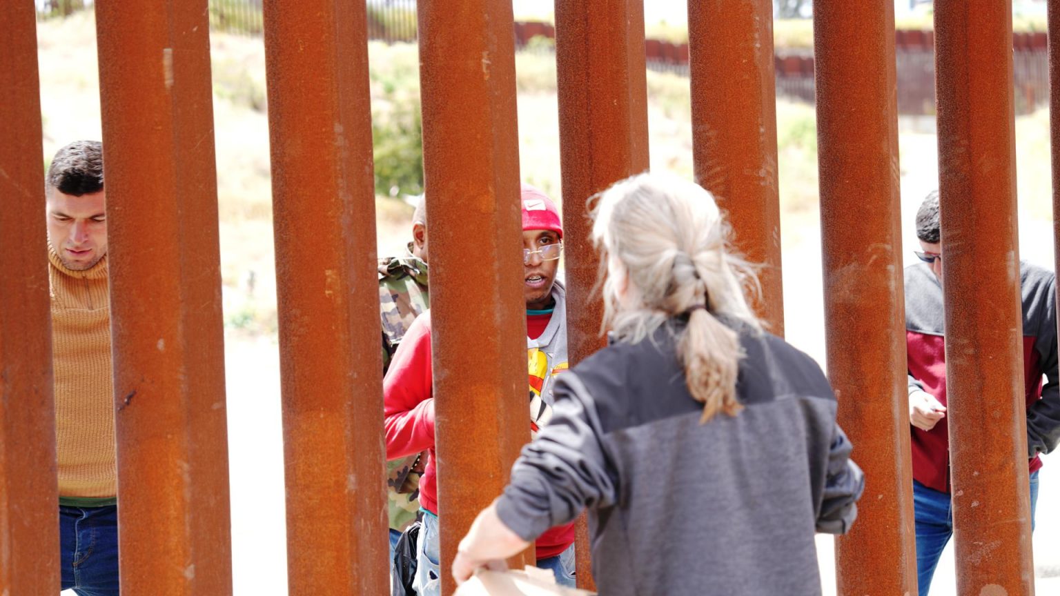 Un hombre habla con padres de familias que se quedaron al otro lado de la valla fronteriza que separa EE.UU. de México, hoy, en San Diego, California (EE.UU.). EFE/ Manuel Ocaño