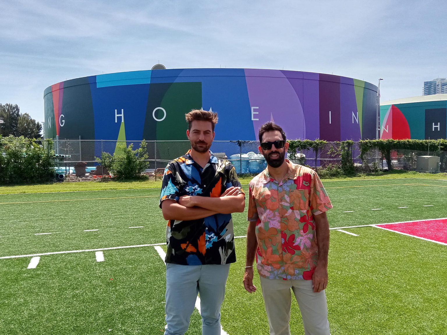 Los miembros del grupo multidisciplinar español Boa Mistura, Juan Jaume (i) y Pablo Ferreira (d), posan para EFE frente a los dos tanques de agua que pintaron junto a las instalaciones de una escuela secundaria, hoy en Miami Beach, Florida (EE. UU.). EFE/Alfonso Rodríguez