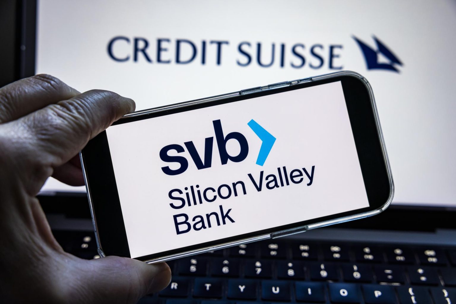 Una foto ilustrativa muestra el logo de Silicon Valley Bank (SVB) en un dispositivo móvil frente a un portátil con el logo de Credit Suisse en Washington, DC, EEUU. Imagen de archivo. EFE/EPA/JIM LO SCALZO