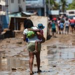 Una mujer carga a un niño mientras camina sobre una calle cubierta de lodo en Leogane (Haití). EFE/ Johnson Sabin