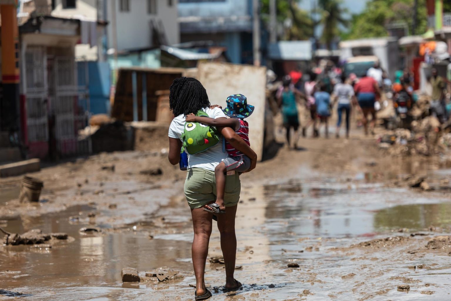 Una mujer carga a un niño mientras camina sobre una calle cubierta de lodo en Leogane (Haití). EFE/ Johnson Sabin