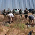 El fundador del Jardín Binacional,  Daniel Watman (c-espaldas), retira hoy junto a la activista Michenee Hoctor (d) la maleza seca de dicho espacio, que ha permanecido acordonado con una cinta amarilla que dice "manténganse fuera", en la frontera con México en San Diego, California (EE.UU). EFE/Manuel Ocaño