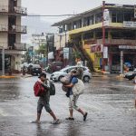 Personas caminan por una calle encharcada debido a las fuertes lluvias en el balneario de Acapulco, estado de Guerrero (México). EFE/David Guzmán