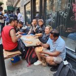 Inmigrantes comen pizza donada mientras hacen fila en espera de ser enviados a un albergue y con la esperanza de tener pronto un empleo, en Nueva York (EE.UU.). EFE/ Ruth Hernández Beltran