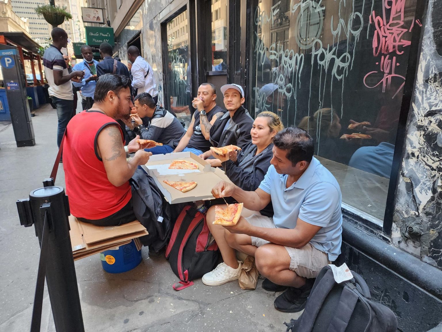 Inmigrantes comen pizza donada mientras hacen fila en espera de ser enviados a un albergue y con la esperanza de tener pronto un empleo, en Nueva York (EE.UU.). EFE/ Ruth Hernández Beltran