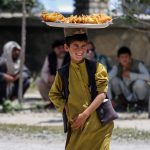 Un niño afgano vende bocadillos en una carretera en vísperas del segundo aniversario de la toma de posesión del gobierno en Kabul, Afganistán. EFE/SAMIULLAH POPAL