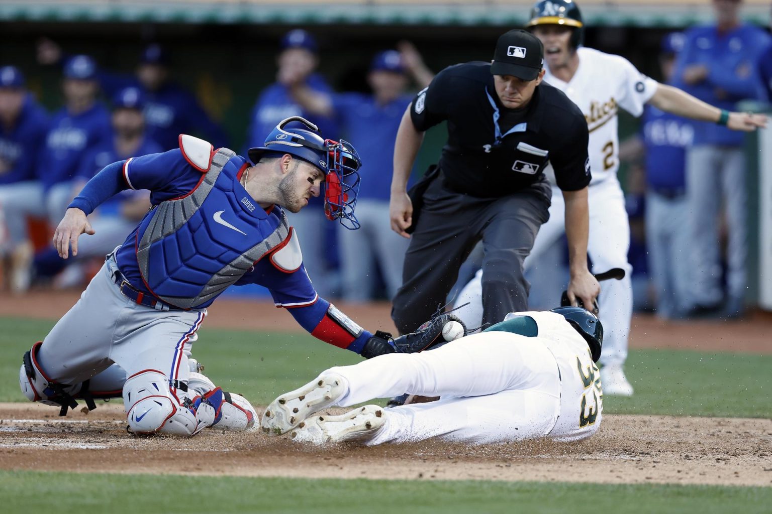 JJ Bleday (d - abajo), de los Atléticos de Oakland, fue registrado este lunes, 7 de agosto, al barrerse sobre el plato para anotar una carrera, ante la mirada del receptor de los Rangers de Texas, Mitch Garver (i), y del juez Adam Beck (c), durante un partido de la MLB, en el estadio Alameda County, en Oakland (California, EE.UU.). EFE/John G. Mabanglo