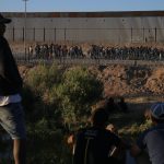 Fotografía de archivo de unos migrantes que esperan cerca de la puerta 42 del muro fronterizo en Ciudad Juárez, mientras integrantes de la Guardia Nacional del Estado de Texas, rodean con barricadas de púas la línea divisoria entre Ciudad Juárez y El Paso. EFE/Luis Torres