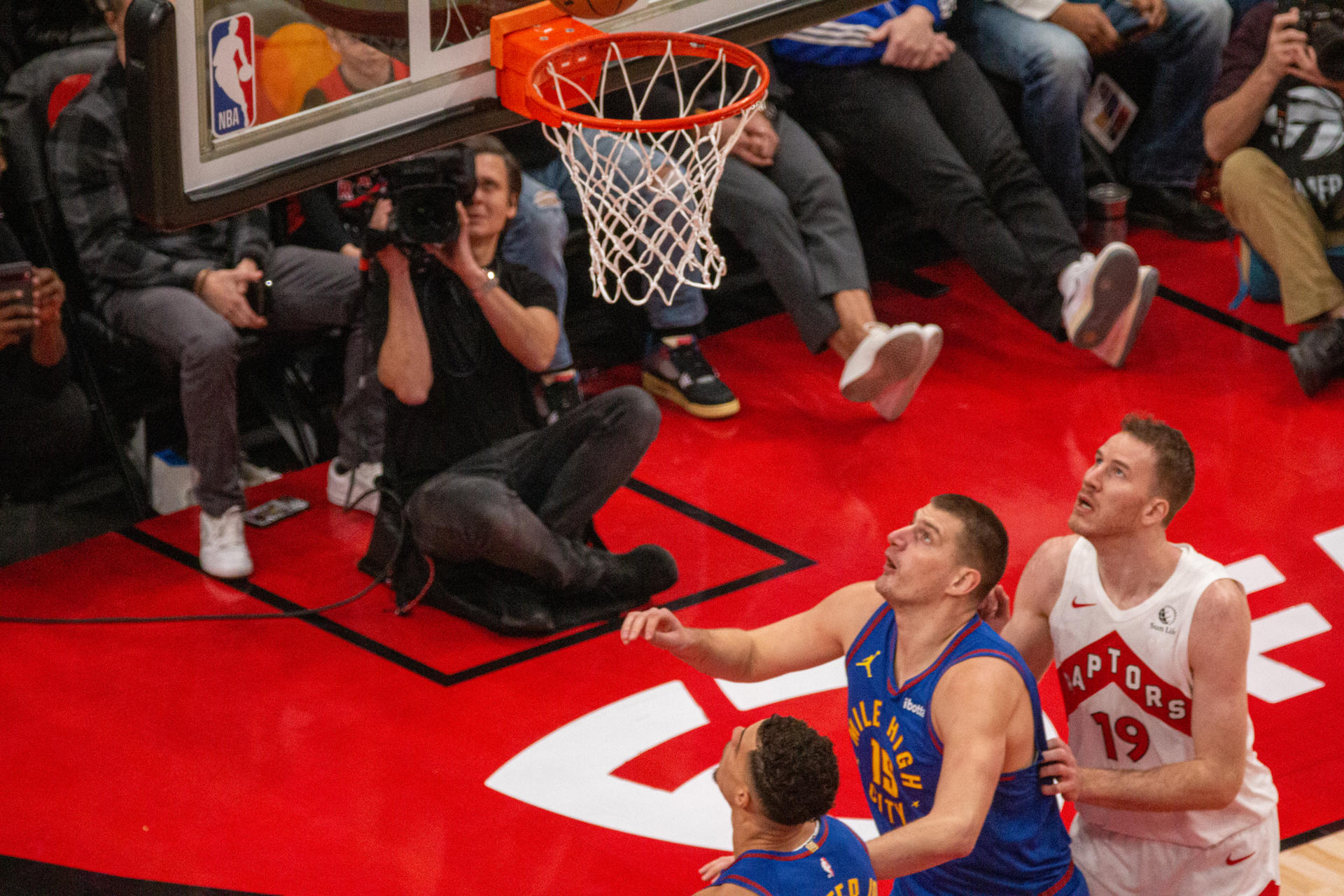 Nikola Jokic (c), pívot serbio de los Nuggets de Denver, fue registrado este miércoles, 20 de diciembre, al observar una canasta que Jakob Poeltl (d), de los Raptors de Toronto, les anota durante un partido de la NBA, en el coliseo Scotiabank Arena, en Toronto (Canadá). EFE/Julio César Rivas
