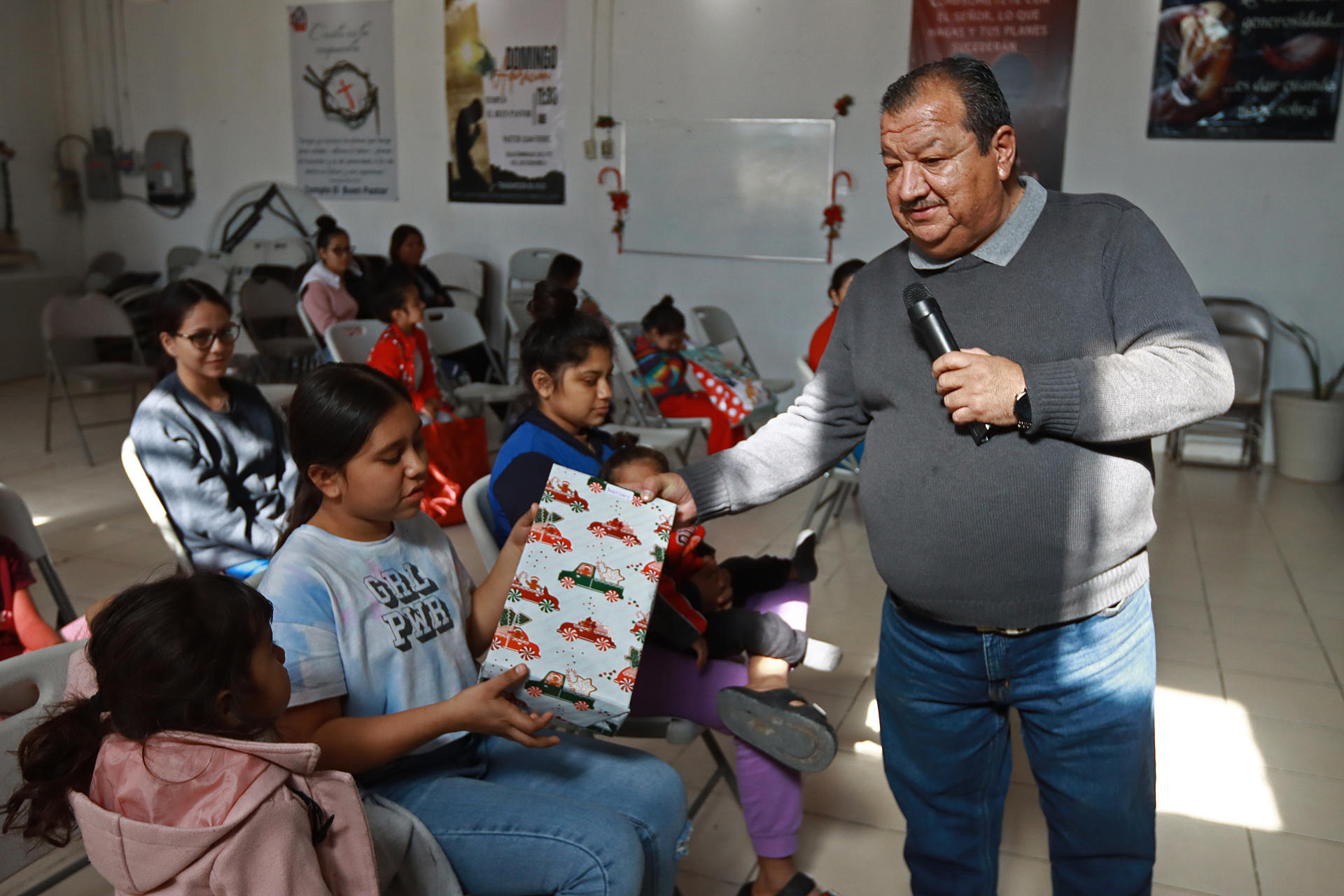 El pastor Juan Fierro (d) reparte regalos a migrantes que pasan la Navidad en el albergue 'El buen samaritano', el 24 de diciembre de 2023, en Ciudad Juárez Chihuahua (México). EFE/ Luis Torres
