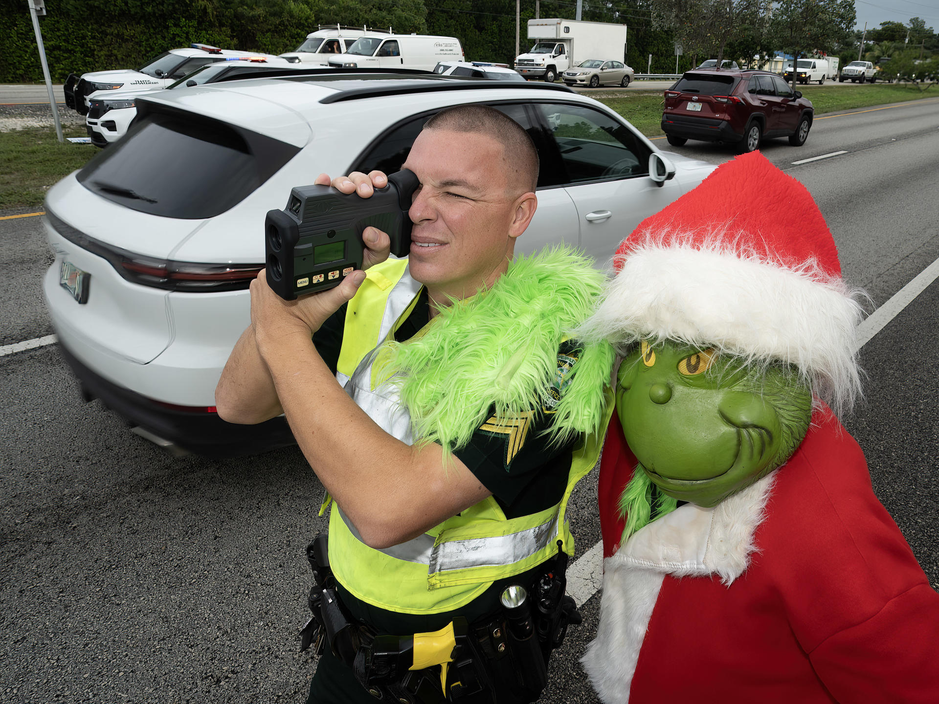 Fotografía cedida por la Oficina de noticias de los Cayos de Florida donde aparece el coronel de la Oficina del Alguacil del Condado de Monroe, Lou Caputo (d), disfrazado del duende 'Grinch', apoyándose en el hombro del sargento James Hager (i), mientras este usa un dispositivo de medición láser para verificar la velocidad de los automovilistas que viajan por la autopista cercana a la escuela primaria Key Largo hoy viernes en Cayo Largo, Florida. EFE/Andy Newman/Florida Keys News Bureau /SOLO USO EDITORIAL /NO VENTAS /SOLO DISPONIBLE PARA ILUSTRAR LA NOTICIA QUE ACOMPAÑA /CRÉDITO OBLIGATORIO
