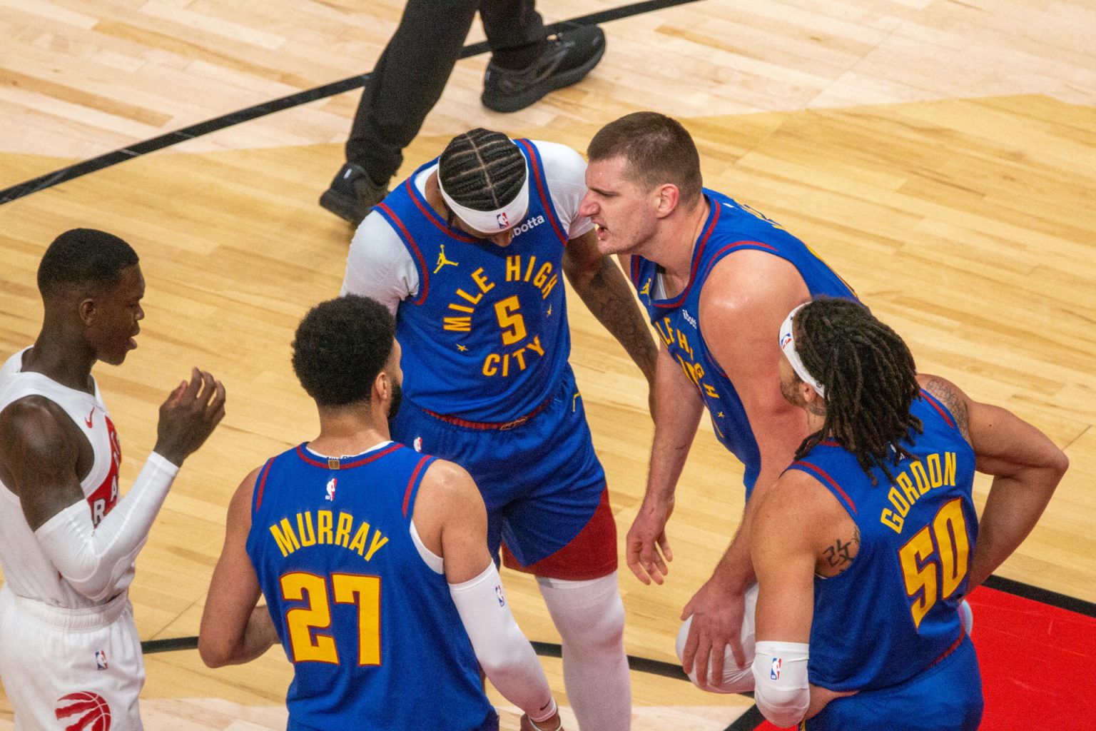 Nikola Jokic (d), pívot serbio de los Nuggets de Denver, fue registrado este miércoles, 20 de diciembre, rodeado por varios compañeros y por Dennis Schroder (i), de los Raptors de Toronto, durante un partido de la NBA, en el coliseo Scotiabank Arena, en Toronto (Canadá). EFE/Julio César Rivas