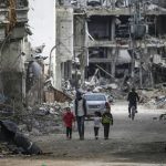 Una familia palestina camina entre la destrucción en el campo de refugiados de Al Bureije (Gaza) este martes. . EFE/MOHAMMED SABER