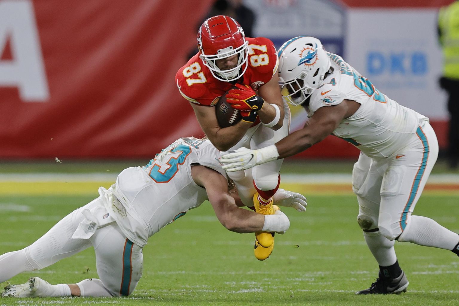 Fotografía de archivo en donde se observa a Travis Kelce (c) de los Kansas City Chiefs siendo abordado por el linebacker de los Miami Dolphins Andrew Van Ginkel (i) y el tackle defensivo de los Miami Dolphins Christian Wilkins (d) durante un juego de la NFL. EFE/EPA/RONALD WITTEK