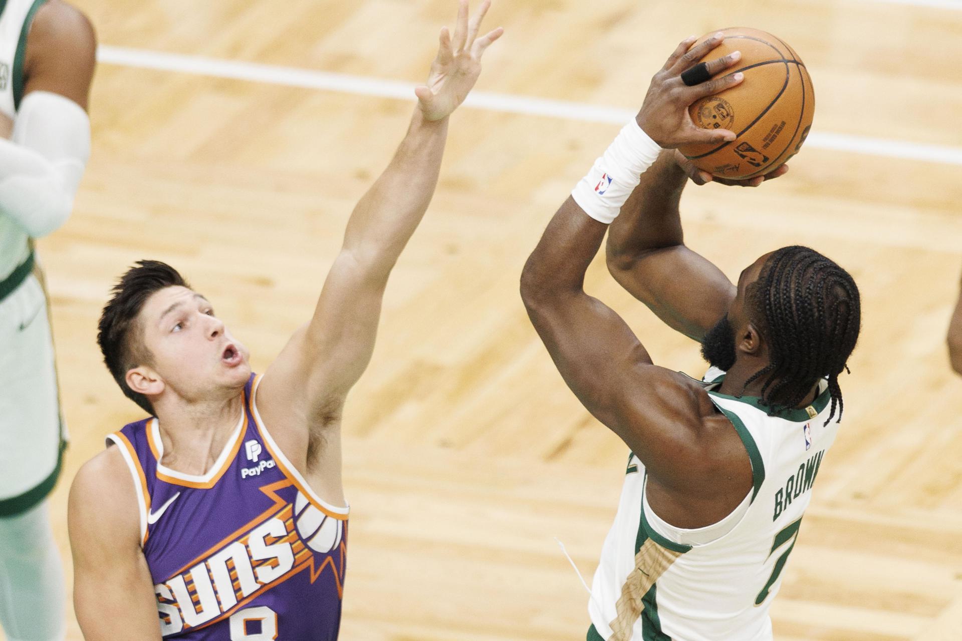 Jaylen Brown (d), guardia de los Celtics de Boston, fue registrado este jueves, 14 de marzo, al intentar un tiro de larga distancia, ante la marca de Grayson Allen (i), guardia de los Suns de Phoenix, durante un partido de la NBA, en el coliseo TD Garden, en Boston (Massachusetts, EE.UU.). EFE/CJ Gunther
