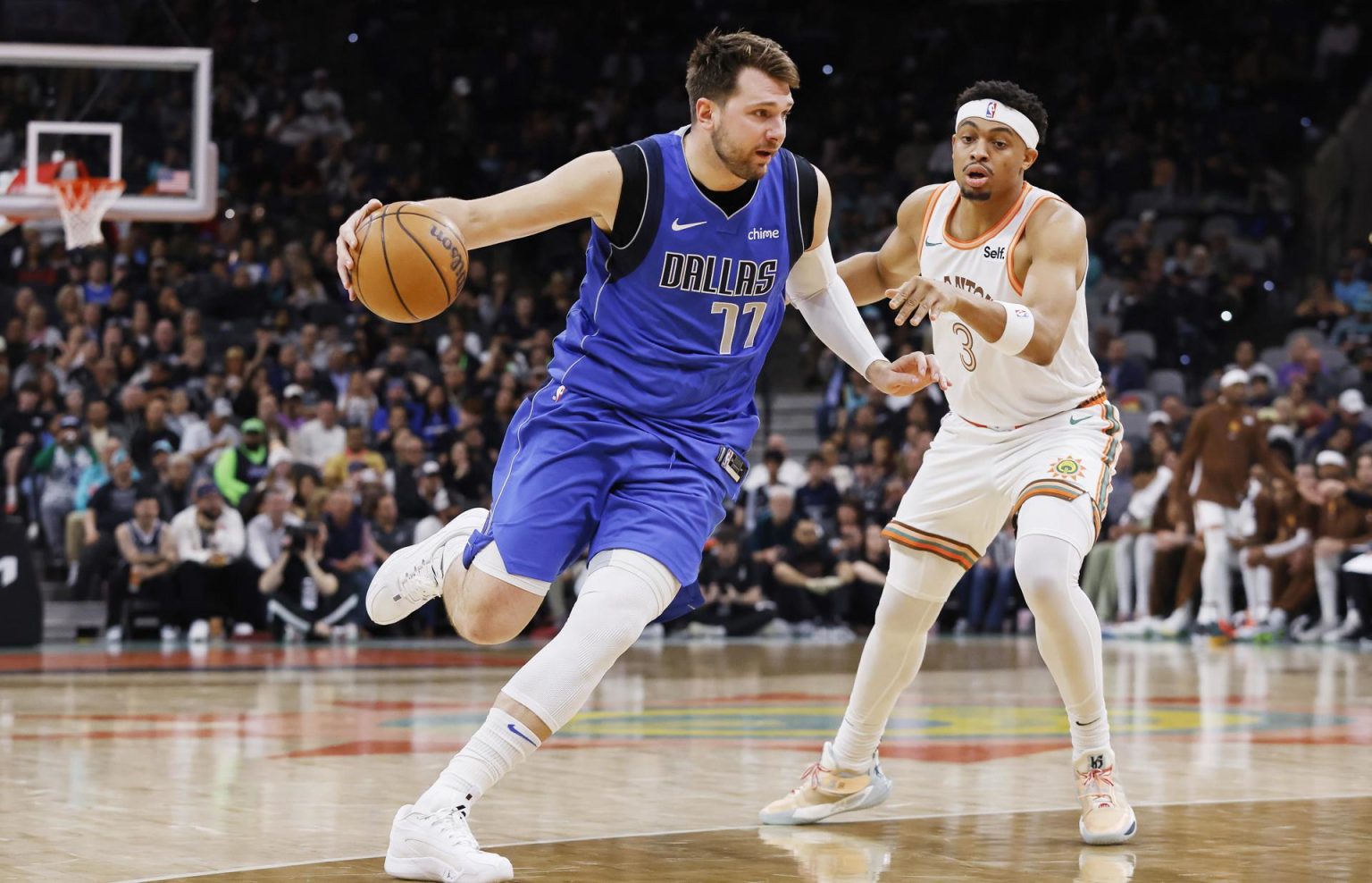 El esloveno Luka Doncic (c), escolta estrella de los Mavericks de Dallas, fue registrado este martes, 19 de marzo, al intentar superar la marca de Keldon Johnson (d), de los Spurs de San Antonio, durante un partido de la NBA, en San Antonio (Texas, EE.UU.). EFE/Adam Davis