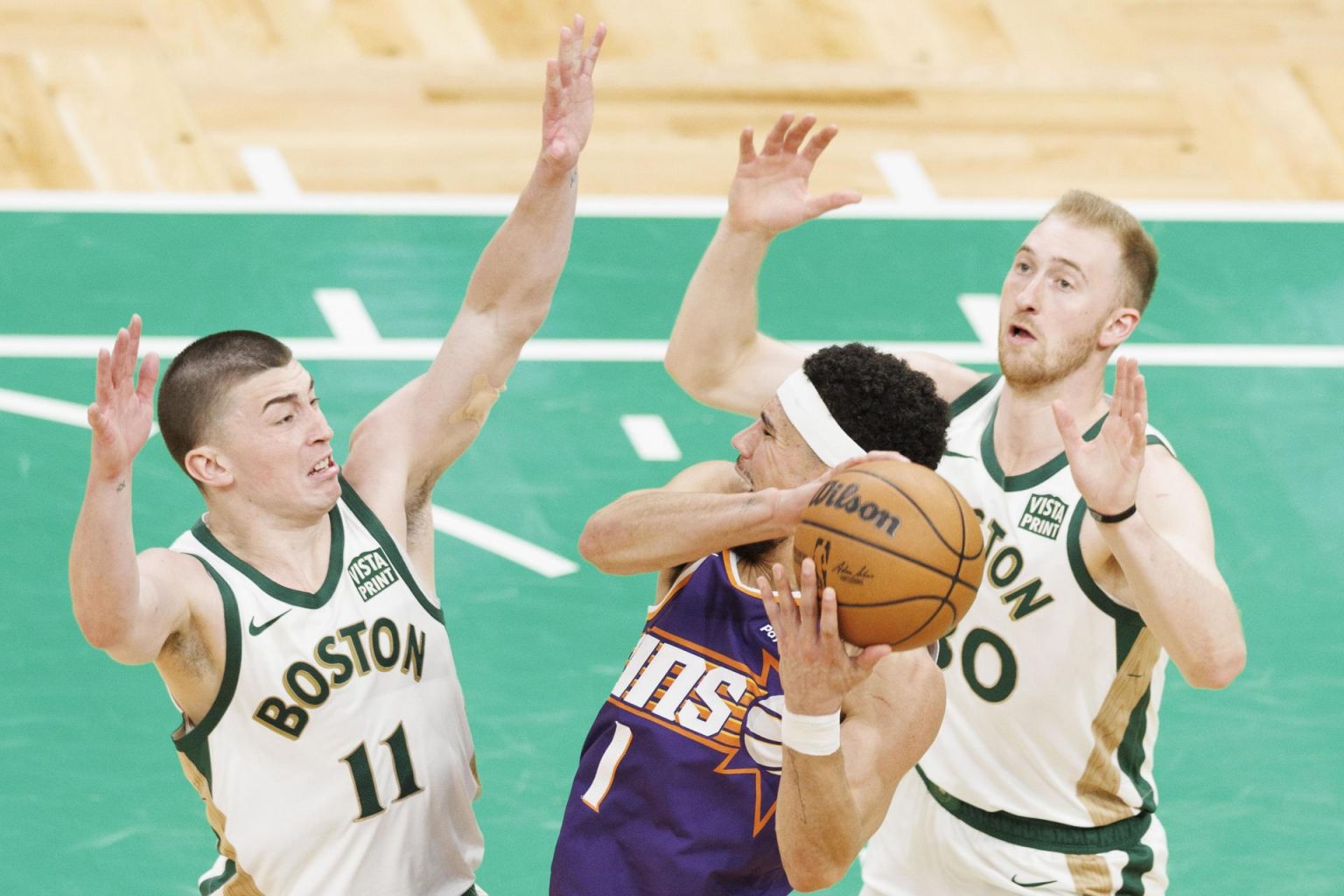 Devin Booker (c), escolta del los Suns de Phoenix, fue registrado este jueves, 14 de marzo, al intentar superar la marca de Payton Pritchard (i) y Sam Hauser, de los Celtics de Boston, durante un partido de la NBA, en el coliseo TD Garden, en Boston (Massachusetts, EE.UU.). EFE/CJ Gunther