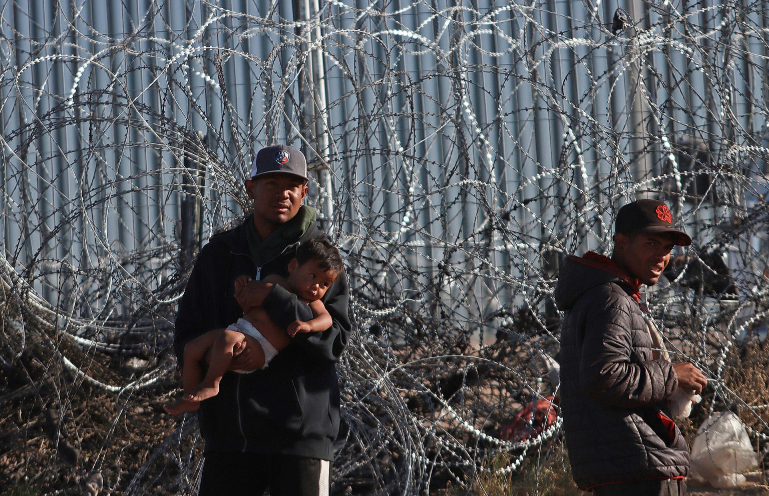 Migrantes permanecen junto a una cerca de alambres en la frontera que divide a México de los Estados Unidos, este jueves en Ciudad Juárez (México). EFE/Luis Torres