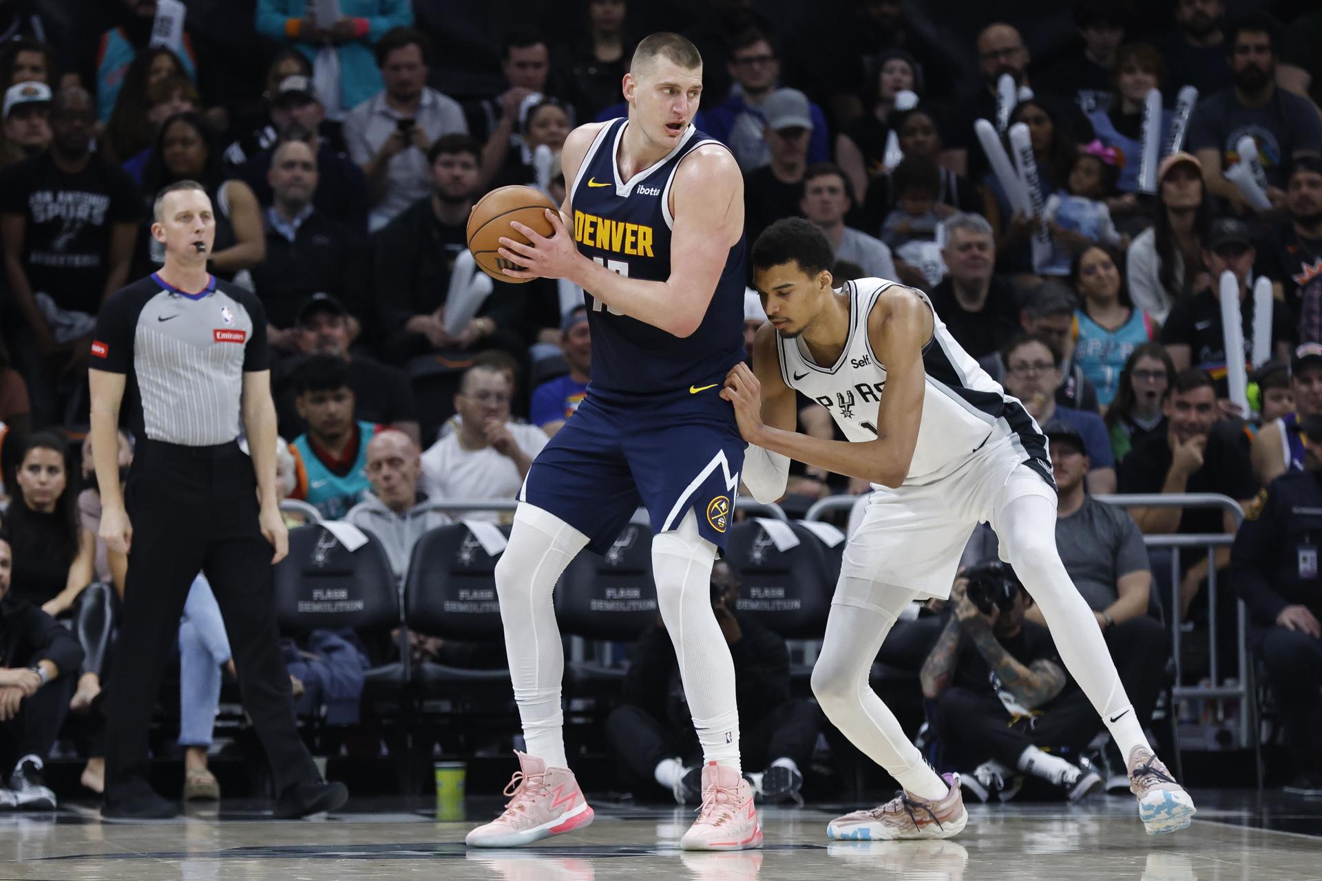 El serbio Nikola Jokic (c), pívot estrella de los Nuggets de Denver, fue registrado este viernes, 15 de marzo, al intentar superar la marca del francés Victor Wembanyama, de los Spurs de San Antonio, durante un partido de la NBA, en Austin (Texas, EE.UU.). EFE/Adam Davis
