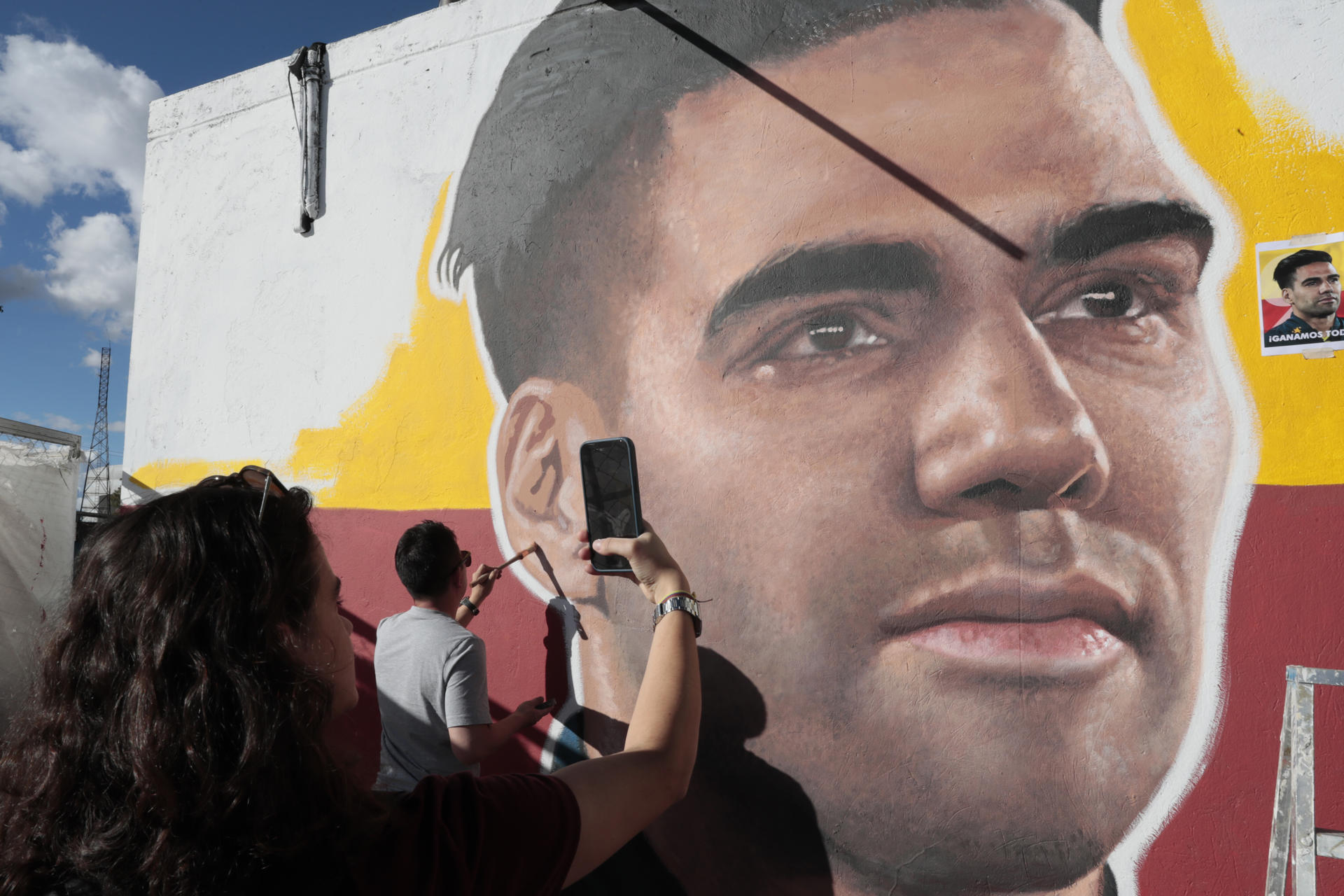 Una mujer fue registrada este martes, 2 de julio, al tomarle una fotografía al artista Emerson Cáceres, conocido como Cacerolo, al pintar un mural con el rostro del futbolista colombiano Radamel Falcao García, en una de las paredes exteriores del estadio Nemesio Camacho ' El Campín', en Bogotá (Colombia). EFE/Carlos Ortega
