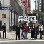 Personas pasan junto a una pancarta que dice 'Israel está matando de hambre a los niños palestinos' este lunes, frente de la sede de las Naciones Unidas en Nueva York (EE.UU.). EFE/ Javier Otazu