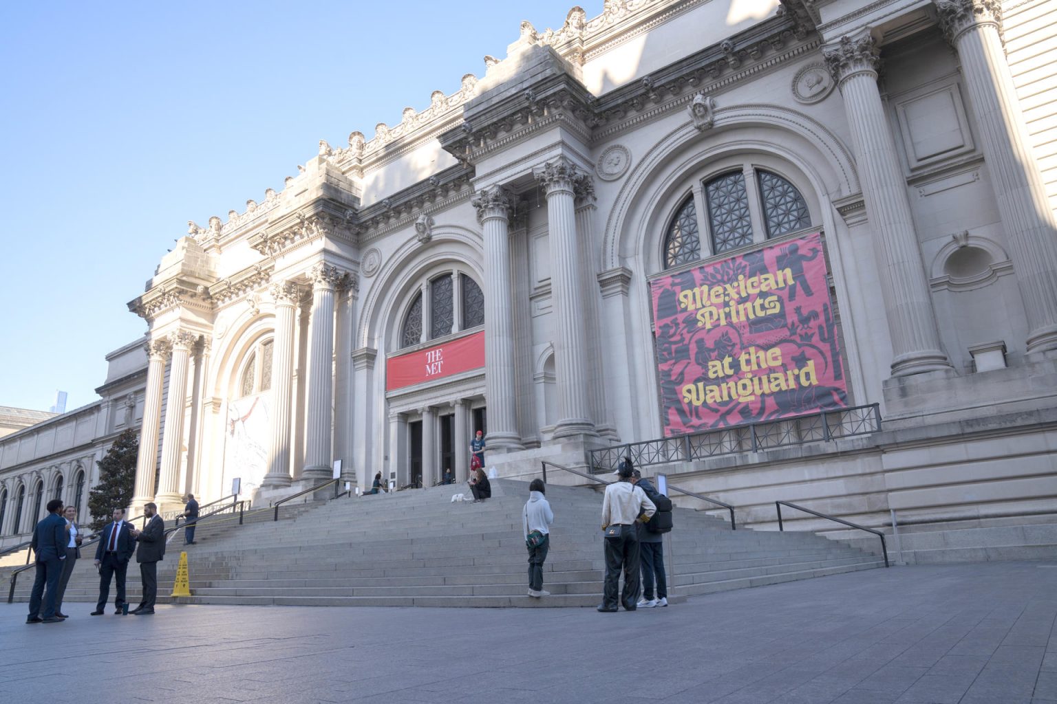 Personas conversan frente a una pancarta de la exposición 'Grabados mexicanos a la vanguardia', colgada en la fachada del Museo Metropolitano (Met), este lunes en Nueva York (Estados Unidos). EFE/Ángel Colmenares