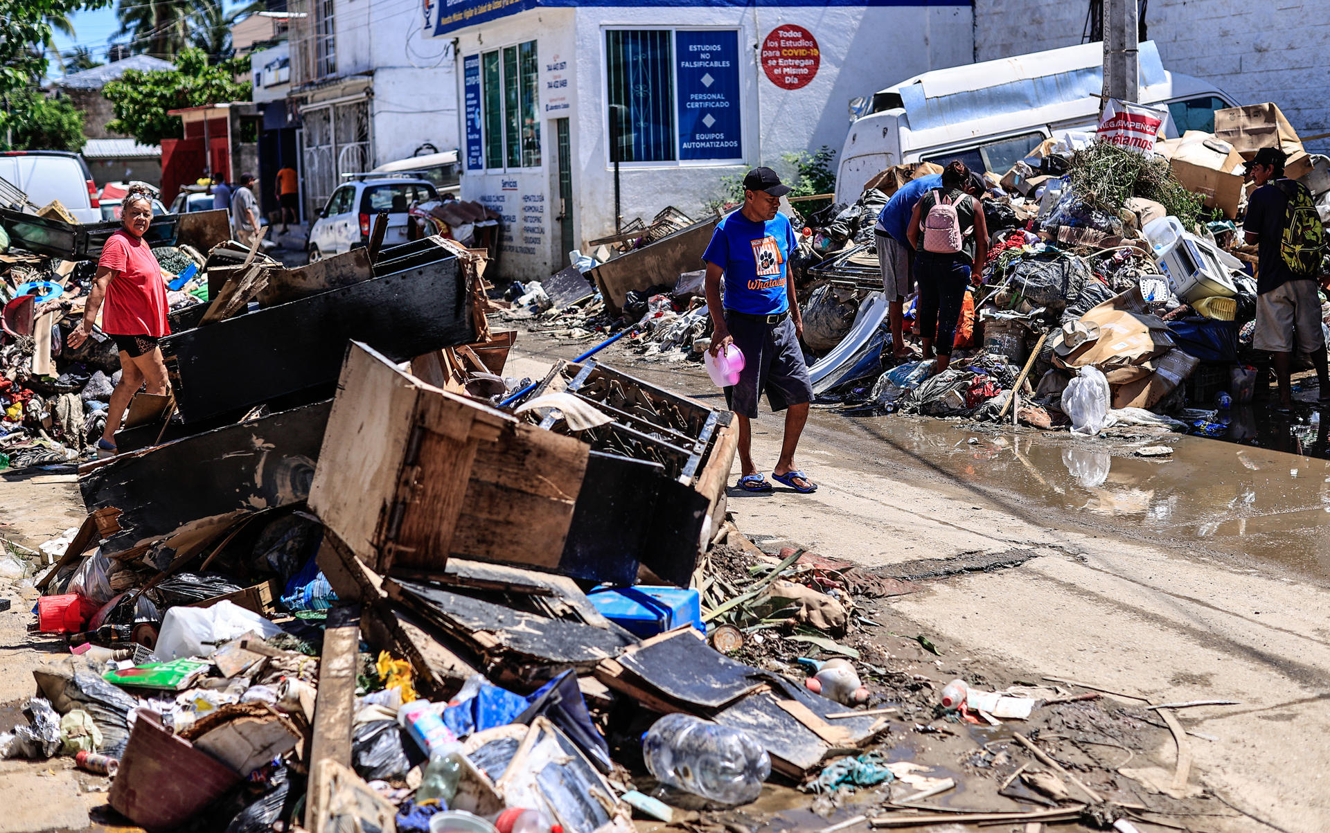 Personas caminan entre basura y enseres domésticos abandonados este lunes en las calles de la unidad habitacional Colosio, una de las más afectadas tras el paso del huracán John, en el balneario de Acapulco (México). EFE/David Guzmán
