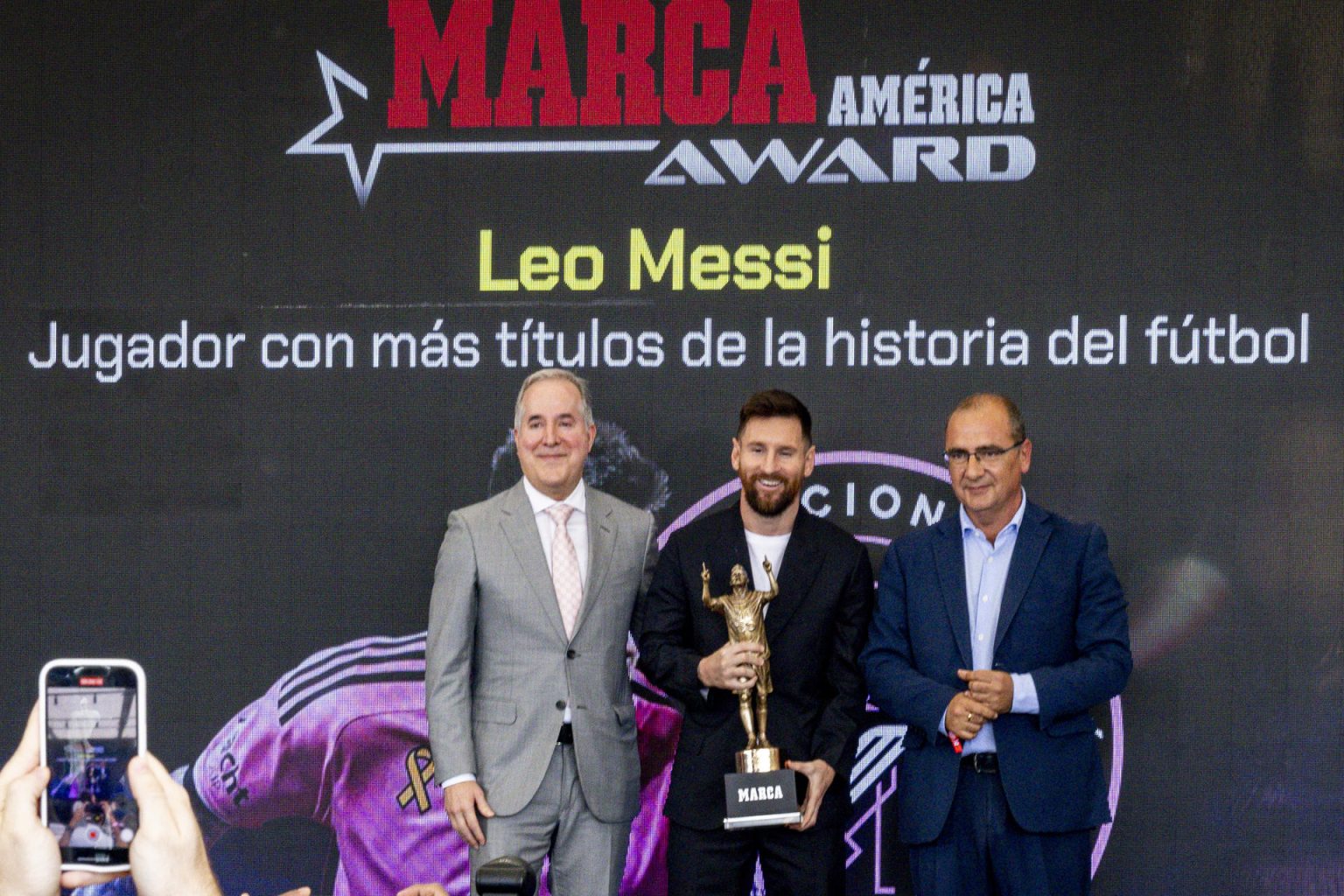 El futbolista argentino Lionel Messi (c) sostiene el trofeo del Premio Marca América junto al dueño del Inter Miami, Jorge Más (i), y el director del diario Marca, Juan Ignacio Gallardo (d), durante una ceremonia, este jueves en el Estadio Chase en Fort Lauderdale, en Florida (Estados Unidos). EFE/ Eva Marie Uzcátegui