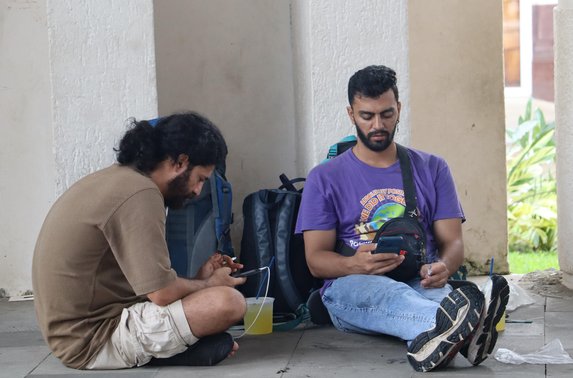 Dos migrantes observan sus celulares en las principales plazas públicas este viernes, en el municipio de Tapachula en Chiapas (México). EFE/Juan Manuel Blanco
