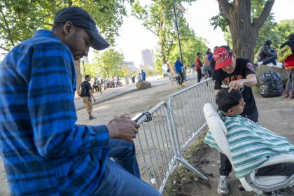 Fotografía que muestra un inmigrante mientras le corta el cabello a otro afuera del refugio de Randall Island en Nueva York (EE.UU.). EFE/Angel Colmenares