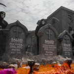 Miembros de organizaciones sociales disfrazados de calaveras posan junto a una ofrenda con esquelas que muestran presuntas cifras de muertes por alcohol, comida chatarra y bebidas azucaradas y tabaco en los últimos 10 años, que colocaron frente a la Secretaría de Salud este jueves, en la Ciudad de México (México). EFE/ Isaac Esquivel