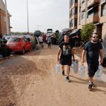 Varias personas con botellas de agua caminan entre los vehículos destrozados en la región valenciana de Paiporta a causa de las fuertes lluvias causadas por la DANA. EFE/Manu Bruque