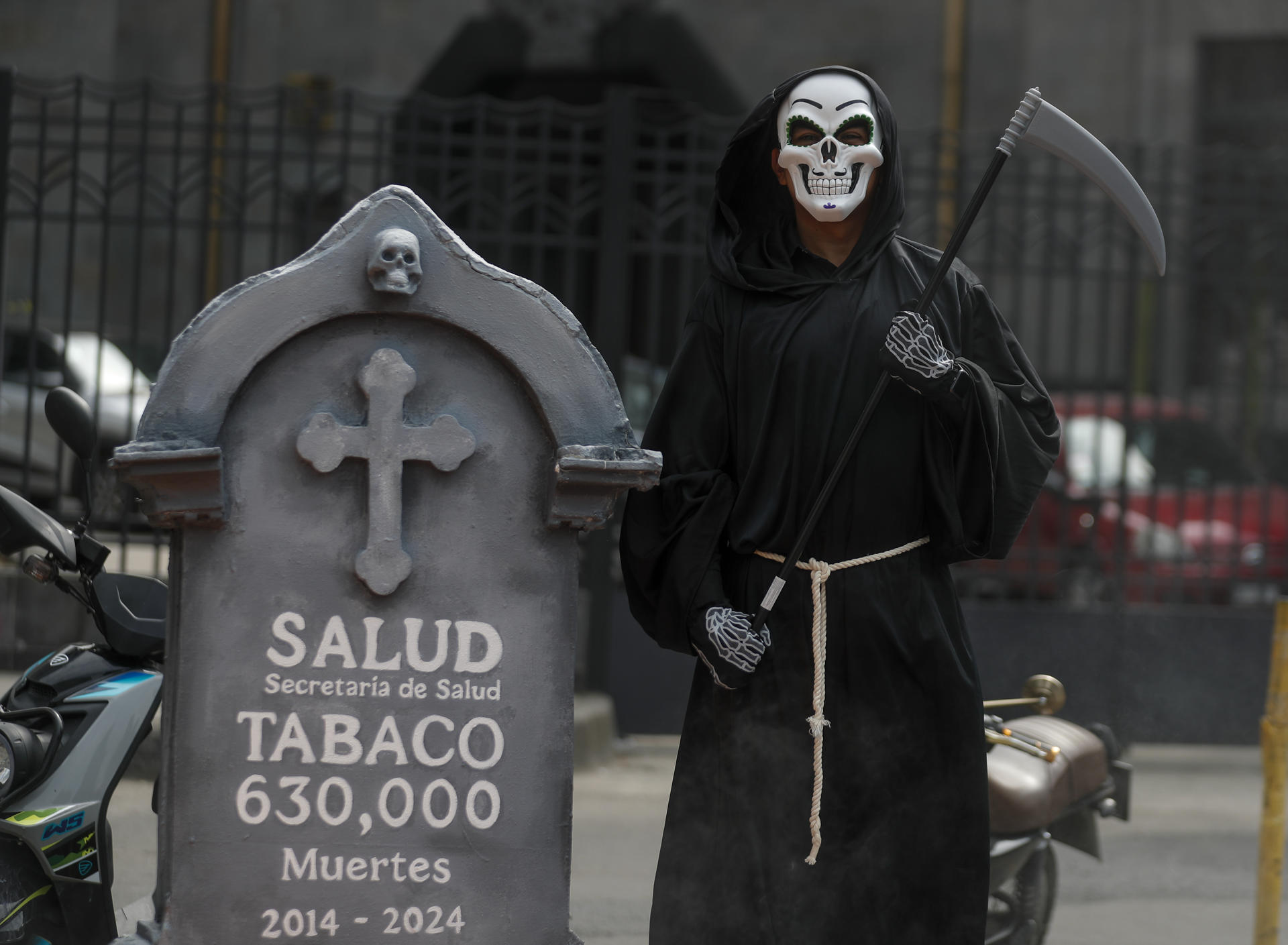 Un miembros de una organización social disfrazado de calavera posa junto a una esquela con una presunta cifra de muertes por tabaco entre 2014 y 2024, en un acto de protesta frente a la Secretaría de Salud este jueves, en la Ciudad de México (México). EFE/ Isaac Esquivel
