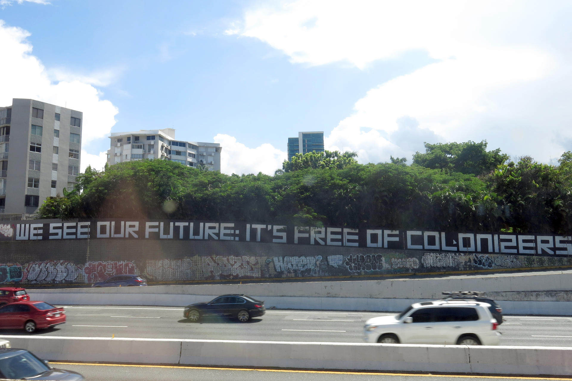 Fotografía del 25 de septiembre de 2024 de vehículos pasar junto a un mural que dice 'Vemos nuestro futuro: libre de colonizadores' en una calle de San Juan (Puerto Rico). EFE/ Esther Alaejos
