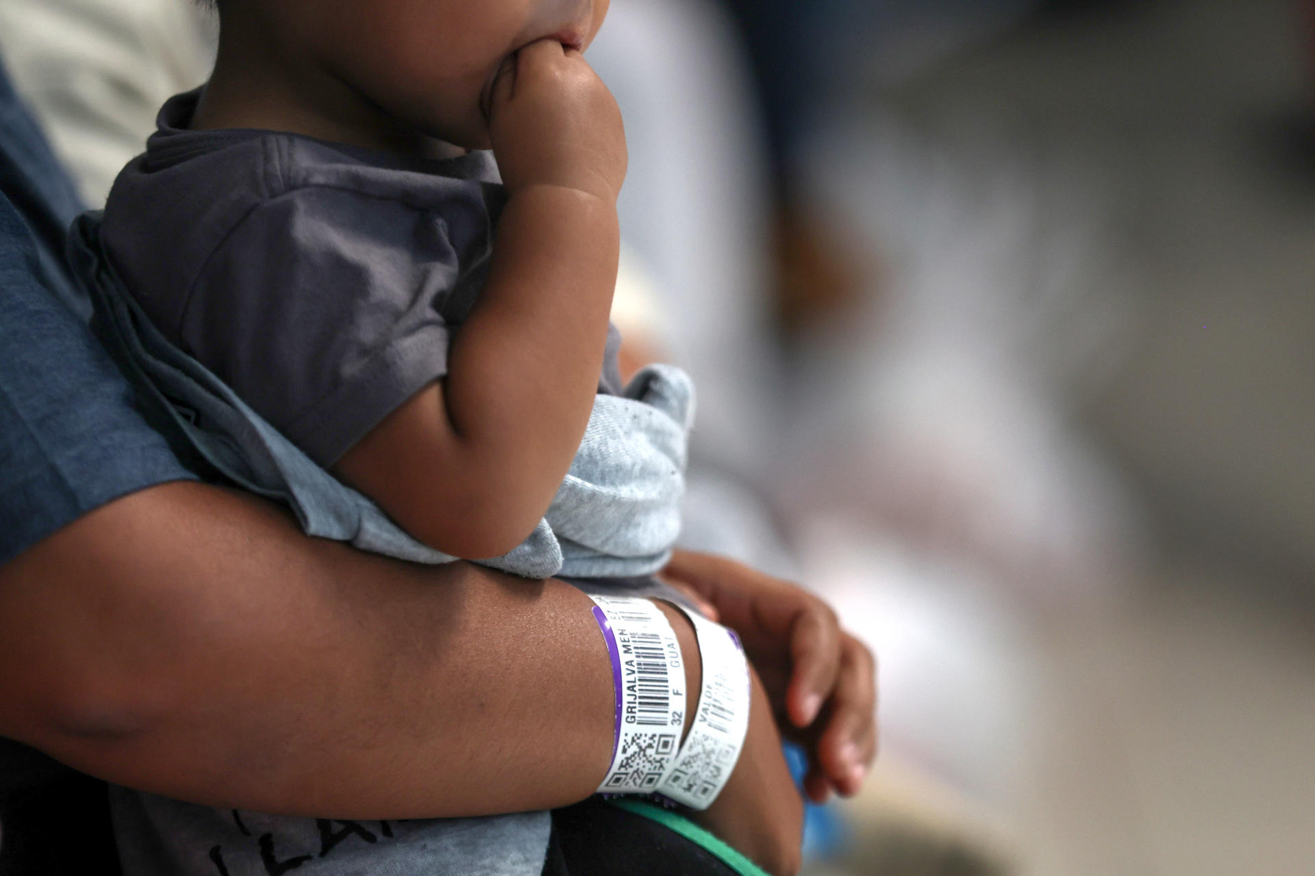 Detalle de los brazos de una persona sosteniendo un bebé que hacen parte de 56 unidades familiares, ingresando al centro de recepción de retornados este viernes en Ciudad de Guatemala (Guatemala). EFE/ Mariano Macz
