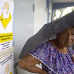 Una mujer se cubre de la lluvia esperando su turno para depositar su voto en un centro de votación en Carolina (Puerto Rico). EFE/Thais Llorca