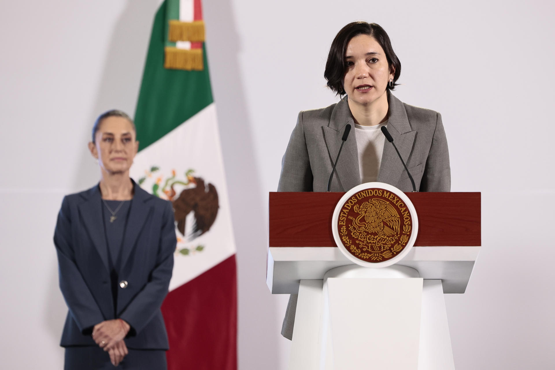 La titular del Secretariado Ejecutivo del Sistema Nacional de Seguridad Pública (SESNSP), Marcela Figueroa (d), habla durante una rueda de prensa de la presidenta de México, Claudia Sheinbaum (atrás), en Palacio Nacional este martes, en la Ciudad de México (México). EFE/José Méndez
